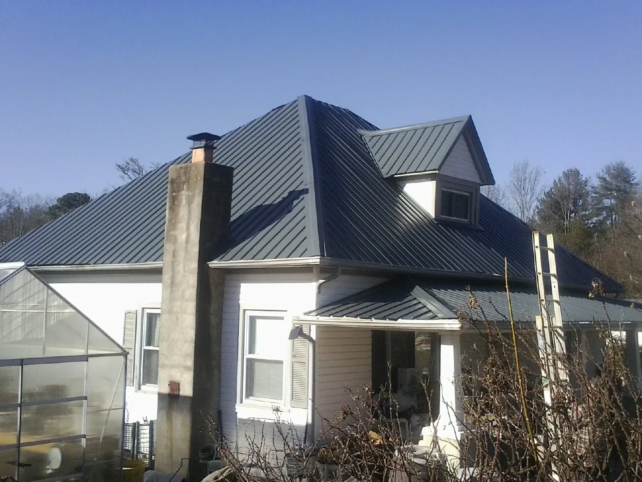 Dark blue standing seam metal roof on a white farmhouse with dormer — Slate & Tile Roof Repair by Roofing Brothers in Rochert