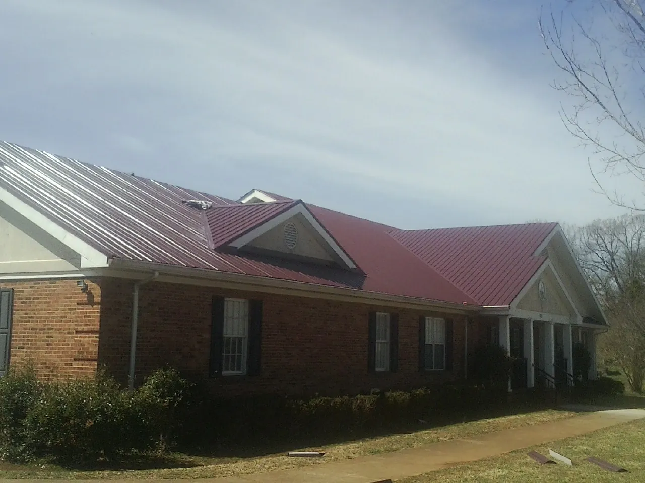 Red metal roof with gabled entries on a long brick building, from a Hail Damage Roof Repair job in Rochert