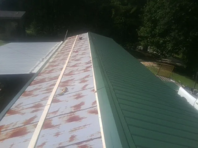 Old rusted panels beside newly installed green metal roofing — Wind Damage Roof Repair by Roofing Brothers in Rochert