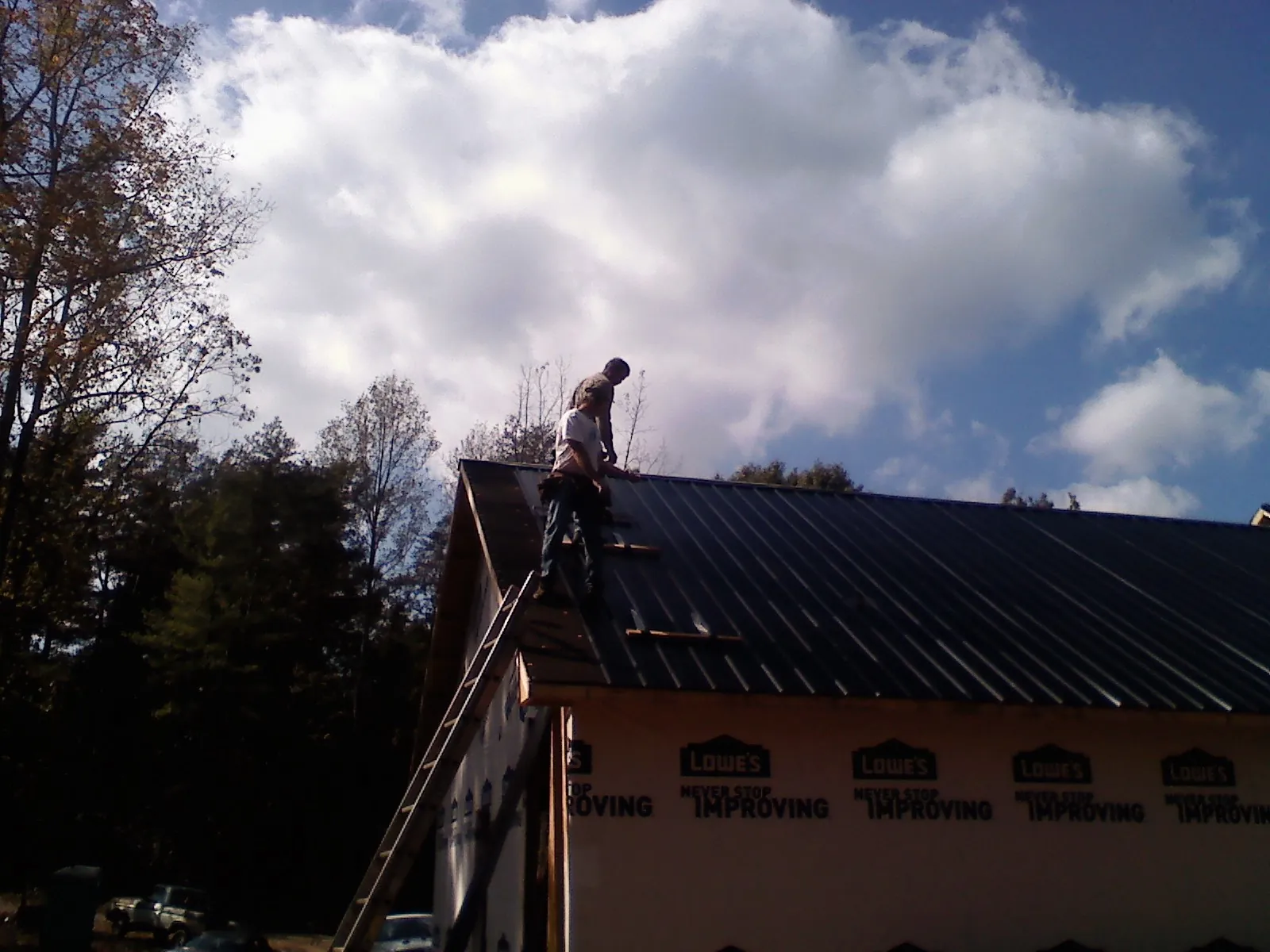 Roofer fastening dark metal panels high against a cloudy sky, from a Roof Inspection job in Rochert
