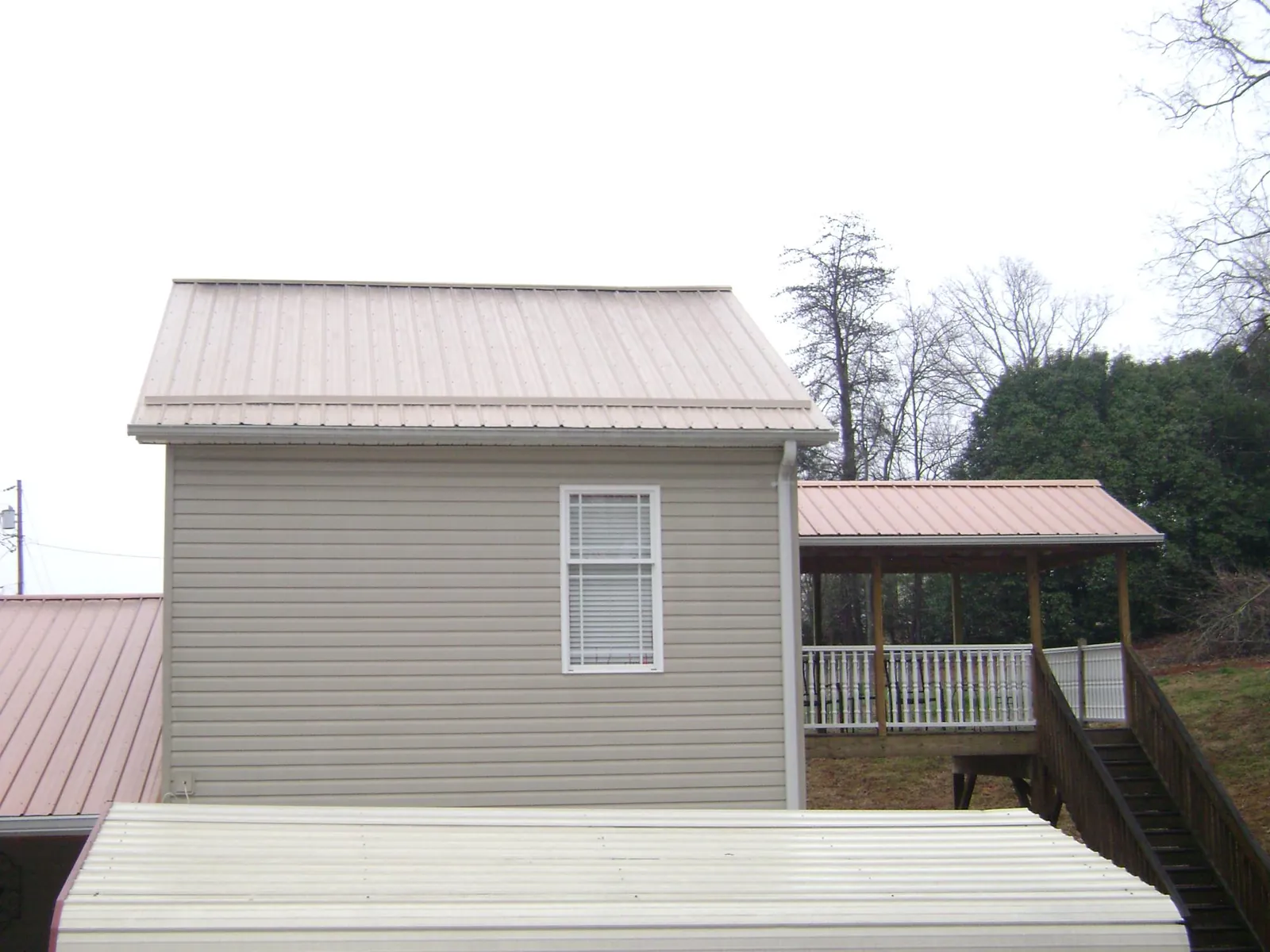 Tan metal roofs on a two story addition and attached porch, from a Roof Replacement job in Rochert